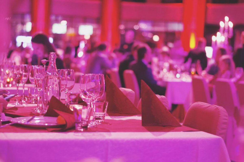 Banquet hall setup before event cleaning with tables, glasses and guests